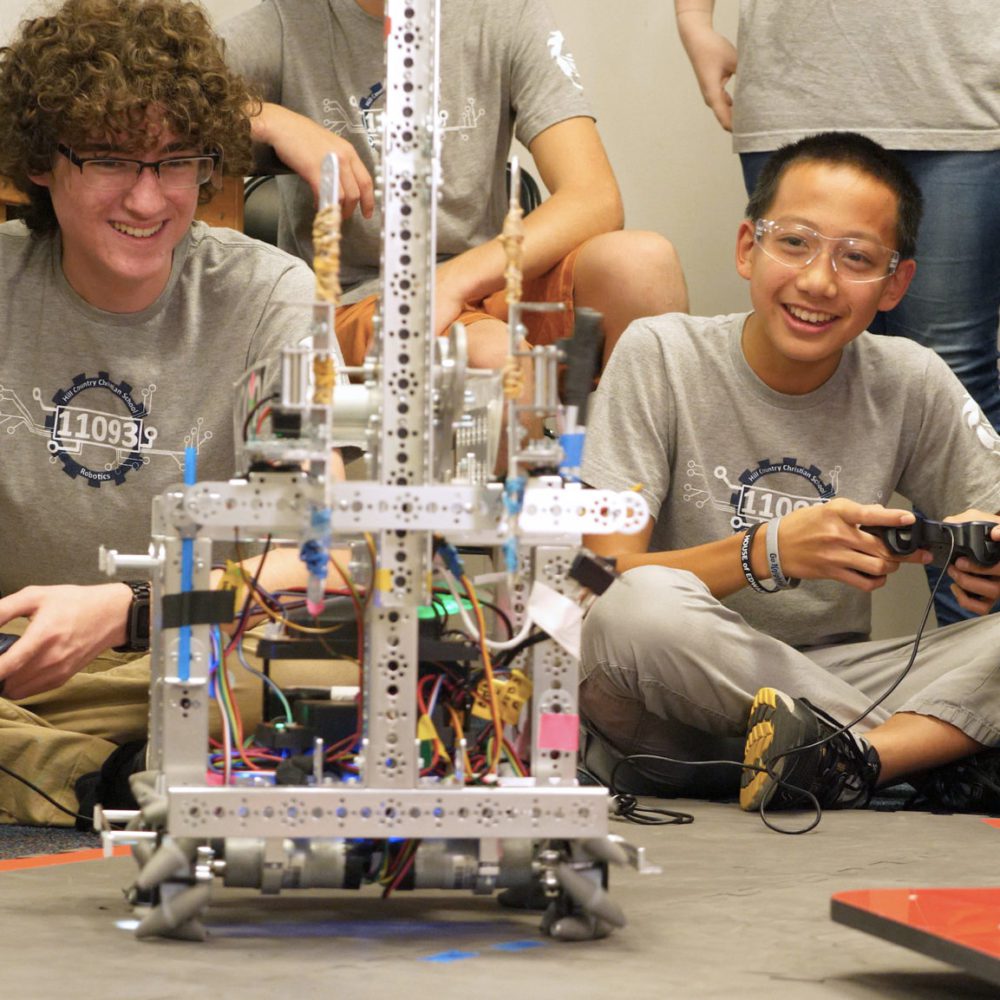 Two students sitting on the floor with remote controls interacting with a robot